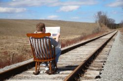 A man sitting on the side of train tracks reading.