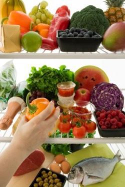 A person is reaching for an orange in the fridge.