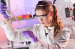 A woman in lab coat and goggles working with liquid.