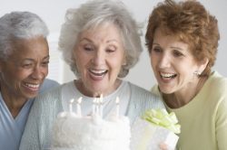 Three women are smiling and holding a cake.